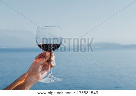 Glass with red wine in woman's hand on blue sea background.