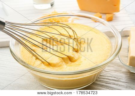 Glass bowl with creamy cheese and corolla on white wooden background
