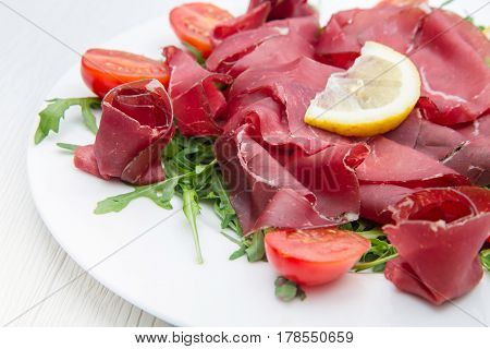 a white dish of bresaola and aragula