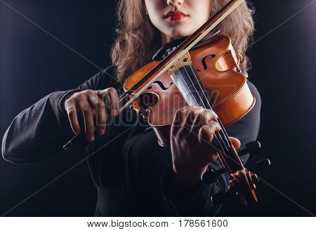 Beautiful young woman playing the violin on dark background