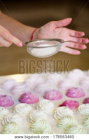 Woman's hands sprinkling with icing sugar a zephyr using sieve. Confectioner sprinkles powdered sugar on marshmallow