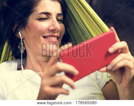 Woman using smart phone with earphone laying on hammock