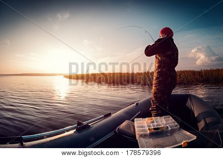 Man fishing from the boat on the lake at sunset