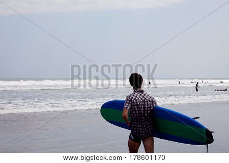 Surfer with surfboard stands on the beach and looking at the sea