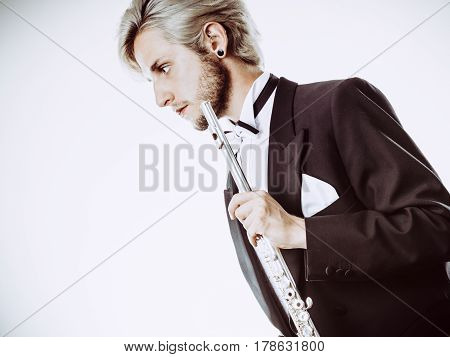 Classical music study concept. Male flutist musician performer playing flute. Young elegant man wearing tailcoat holds instrument
