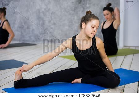 Shot of young women warming up before yoga session. Young people sitting on exercise mat in yoga class