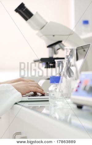 Arbejder i laboratoriet med mikroskop og skrive resultater på laptop, closeup