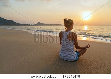 Young woman practices yoga and meditates on the beach at sunrise