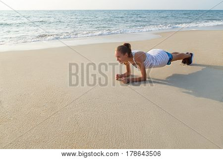 Young woman is doing plank exercise on the beach