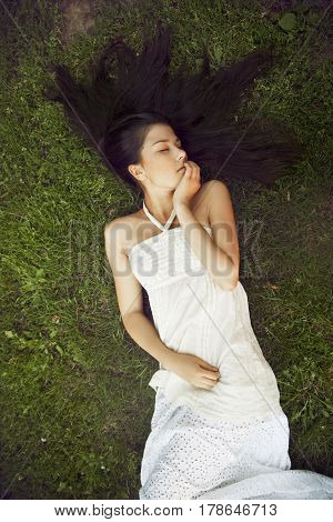 A girl with long dark hair wearing lying on grass