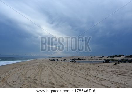 Horizontal landscape of the beach with cars. 4wd cars at Crokers creek (Belmont - Nine Miles - Beach NSW Australia). Redhead Point in the background.