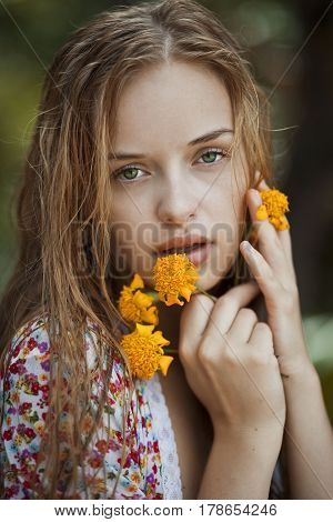 Portrait of a blonde girl with green eyes holding yellow flowers