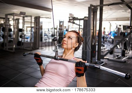 Young fitness woman performing close grip lat pulldown on cable machine