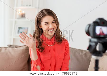 blogging, technology, videoblog, mass media and people concept - happy smiling young woman or blogger with camera recording video and waving hand at home