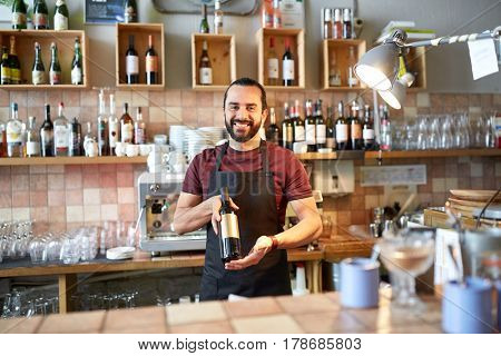 small business, alcohol drinks, people and service concept - happy man or waiter with bottle of red wine at bar