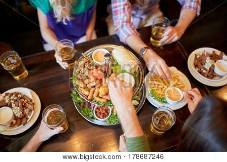 leisure, food, drinks, people and holidays concept - friends eating snack and drinking beer at bar or pub