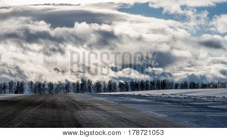 A landscape with the winter forest under the dramatic cloudy and sun