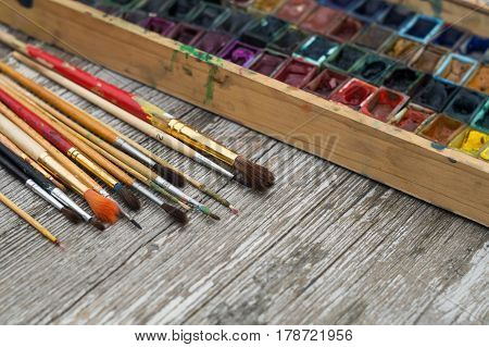 Box with watercolors and brushes on wooden surface