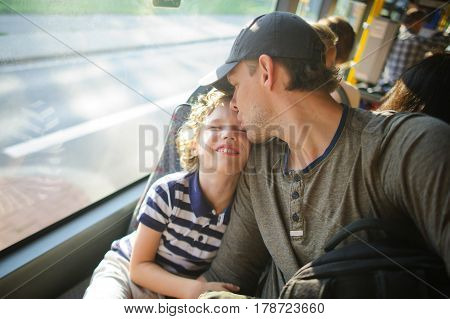 The young man goes by the bus together with the son. The father and the son sit next with each other and communicate with pleasure. On their faces expression of love and joy.