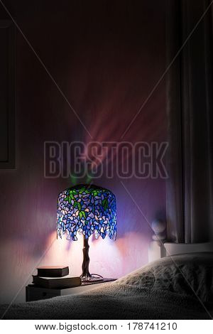 Light reflections in a pretty pink bedroom at night from a Tiffany style lamp. Deep shadows and glowing coloured light from the wisteria design stained glass creates a cosy mood. Copy space.