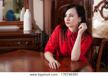 Beautiful Girl Sitting At A Table In A Red Dress,