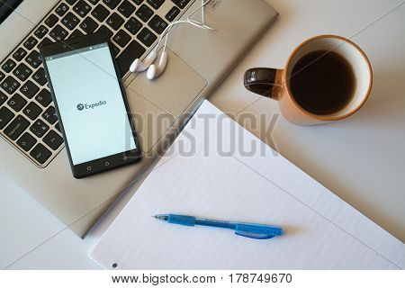 Nitra, Slovakia, march 28, 2017: Expedia application in a mobile phone screen. Workplace with a laptop, an earphones, notepad and coffee.