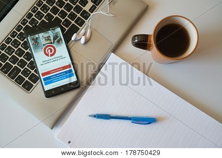 Nitra, Slovakia, march 28, 2017: Pinterest application in a mobile phone screen. Workplace with a laptop, an earphones, notepad and coffee.