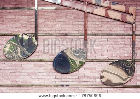 Three metal sixteenth notes as decor on brick wall.