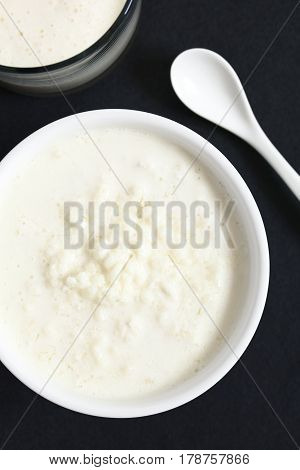 Kefir grains in milk with a glass of fresh kefir drink on the side photographed overhead on slate with natural light (Selective Focus Focus on the top of the kefir grains and the kefir drink)