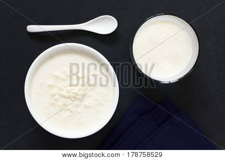 Kefir grains in milk with a glass of fresh kefir drink on the side photographed overhead on slate with natural light (Selective Focus Focus on the top of the kefir grains and the kefir drink)