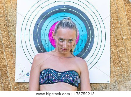 Attractive young smiling beautiful curly blonde hair slim girl fashion portrait in black swimming suit posing looking away calm look in target archery background.