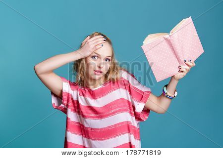 young attractive blond woman holding a pink book on blue background