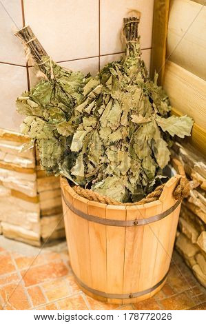 Bath accessories in traditional Russian sauna. Bath brooms from oak in wooden sauna bucket in the russian bath close up. Oak venik for banya.