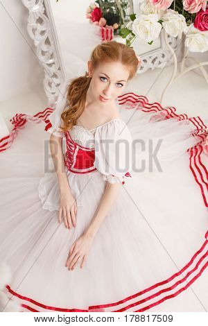 Pretty ballerina in stage costumes and bouquets of spring flowers. Retro dress. She sits on the floor. High angle shooting