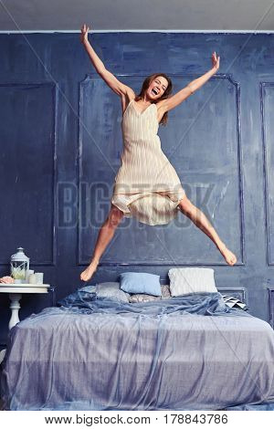 Low angle of an attractive young woman jumping energetically on the bed. Extremely excited woman in nightgown jumping on bed with arms and legs outstretched