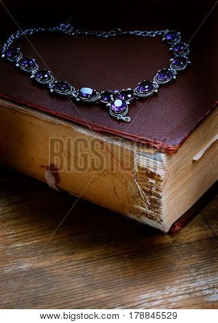 Still life with an old book and ozherelem jewelry from silver with natural stones of violet colour.