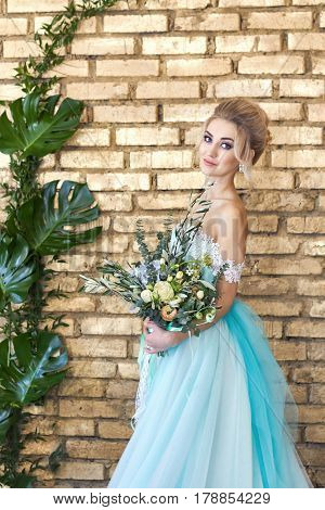 Bride in a beautiful turquoise dress in anticipation of wedding. Blonde in lace dress sea green with a bouquet . Happy bride emotion joy on her face. Beautiful makeup manicures and hairstyles women