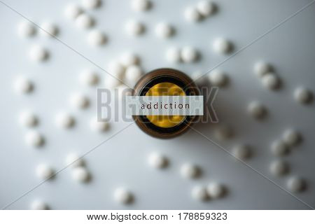 White medicine tablets or pills scattered on a white table and  brown glass medicine bottle on center, with paper on top with the words 
