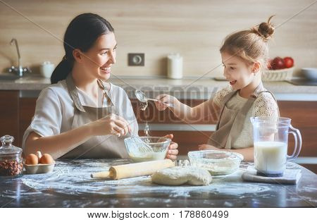 Happy loving family are preparing bakery together. Mother and child daughter girl are cooking cookies and having fun in the kitchen. Homemade food and little helper.
