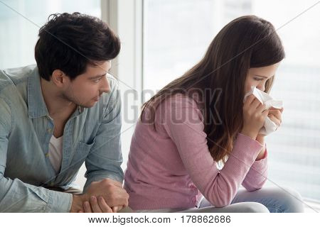 Sad upset girl crying, wiping tears with handkerchief, friend or boyfriend trying to comfort her at home, husband consoling depressed wife, support in difficult situation, compassion or apologize