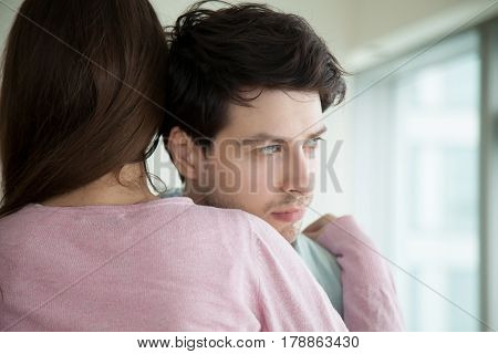 Woman hugging her upset boyfriend, sad guy looking away through the window, loving wife supporting husband, embracing and comforting him, helping to solve business problems, couple reconciliation
