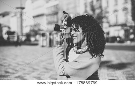 Black and white view of beautiful woman while making shoot on vintage camera greyscale portrait of curly Brazilian lady in coat and sweater using retro camera with copy space for your text message