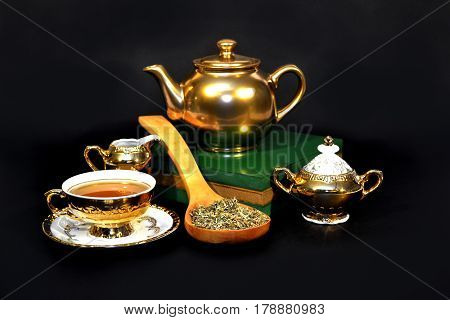 Golden tea set with a spoon full of herbs on on the dark background