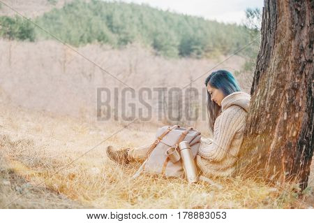 Traveler young woman with backpack and thermos resting near a tree outdoor in sunny day
