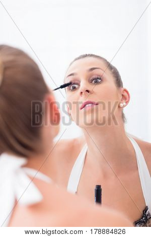 Woman using mascara on her eyelashes in front of bathroom mirror 