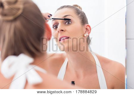 Woman using mascara on her eyelashes in front of bathroom mirror 