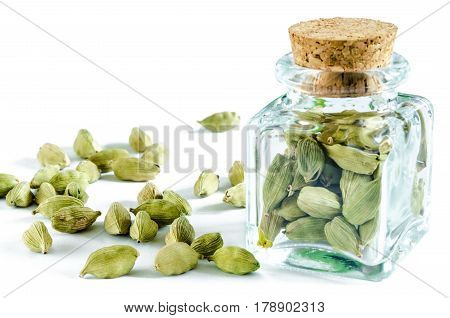 Dry cardamom seeds in glass bottle and heap of cardamom isolated on white background. Closeup macro shot.
