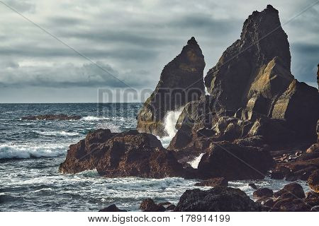 Reynishverfisvegur, Reynisfjara black sand beach with rocks, ocean and dark rain and storm clouds near the village of Vik in Iceland.