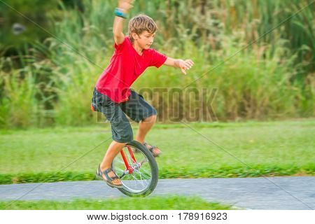 outdoor portrait of young boy riding a unicycle (one wheel bike) on natural background