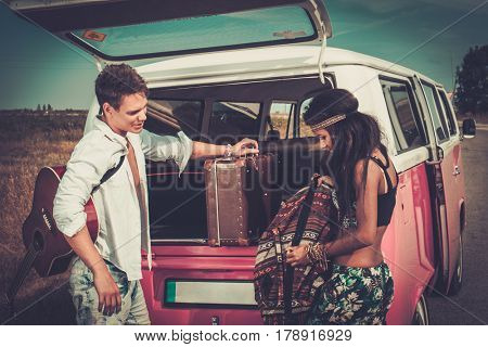 Multi-ethnic hippie couple with guitar packing luggage for a road trip